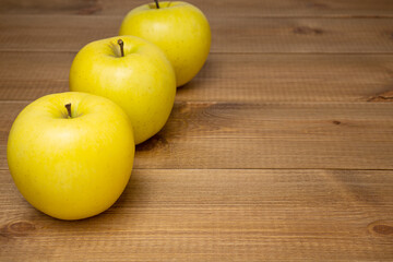 Row of three yellow ripe Golden apples on wooden table. Sweet and juicy fruits.