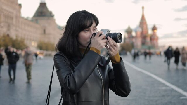 Young woman photographer at the centre of Red Square in Moscow. Handheld shot of happy young asian woman tourist taking pictures on background of Kremlin