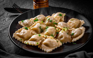 Meat dumplings - russian pelmeni, ravioli with meat in black plate on Dark grey black slate background