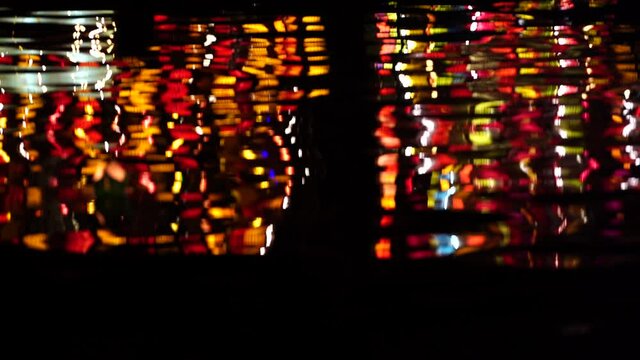 The night river water waves reflects the bright street colorful light, close up. Hoi An, Vietnam