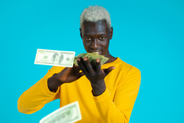 Mixed race man with happy face scatters money. People overspend US currency. African man is flush with dollars on blue studio background.