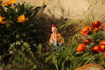 mała  figurka  klowna  ustawiona  w  ogródku  między  kwiatami