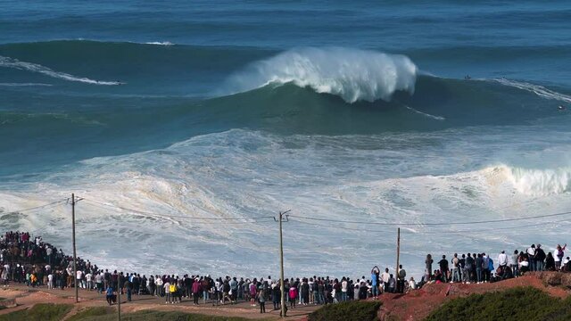 People watching big wave surfers riding giant waves near Praia do Norte beach in Nazare, Portugal. Nazare is famously known for having the largest waves in the world. - Powered by Adobe