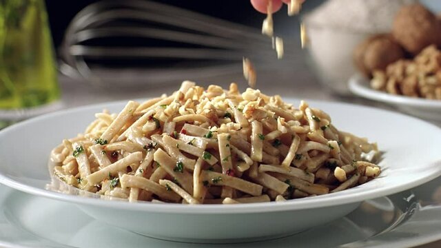 Slow motion spice and walnut pieces are thrown over the Turkish noodles on the serving plate.