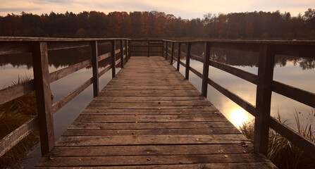 Sun rays falling on the pier on the lake surrounded by forest in autumn colors