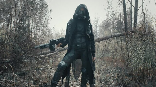 Human of future. Caucasian woman in futuristic clothes and gas mask standing in forest. Dystopian stalker concept, female survivor posing with gun. Post apocalyptic world. Cyberpunk steampunk