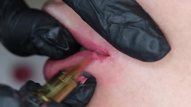 Cosmetologist making lips microblading permanent procedure using tattoo machine and pink pigment