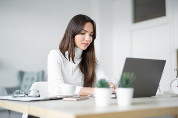 Woman in white sweater sits in front of laptop.