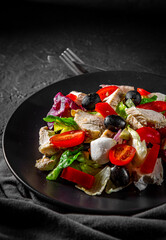 Fresh salad with chicken breast, cheese, black olives,red pepper, lettuce, fresh sald leaves and tomato on a black plate on Dark grey black slate background