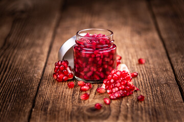 Some fresh preserved Pomegranate seeds on wooden background (selective focus; close-up shot)