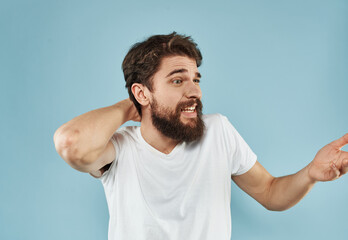 Cheerful guy in a T-shirt with a beard on a blue background holds his hand behind his head