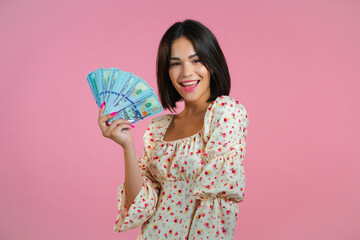 Amazed happy excited woman showing money - U.S. currency dollars banknotes on pink wall. Symbol of success, gain, victory.