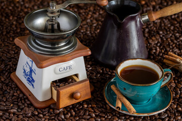A cup of coffee, cinnamon sticks, a coffee mill and a coffee maker on the background of coffee beans. Life style.