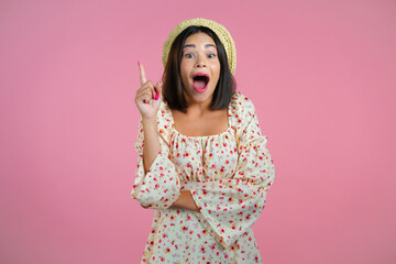 Portrait of young thinking pondering woman having idea moment pointing finger up on pink studio background. Smiling happy showing eureka gesture.