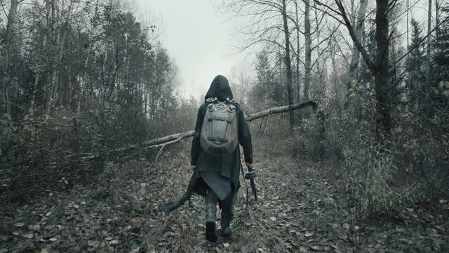 Following shot of woman in military clothes walking along trail in dark forest. Stalker concept, female survivor with gun during nuclear or chemical war. Post apocalyptic world. Dystopian future
