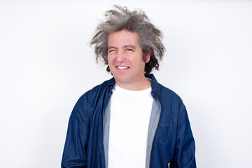 Handsome mature caucasian man with afro grey hair standing over white background blinking his eyes with pleasure having happy expression. Facial expressions and people emotions concept.