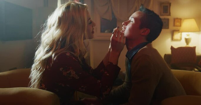Cinematic shot of an young carefree happy smiling homosexual female gay and transgender man couple in love is having fun to making up lips and kissing while sitting on a sofa in living room at home.