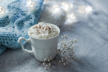 cozy winter composition with cup of hot chocolate, hot cooca cup with knitted sweater and ball lights, girly winter aesthetic photography, blue and white hues and airy atmosphere