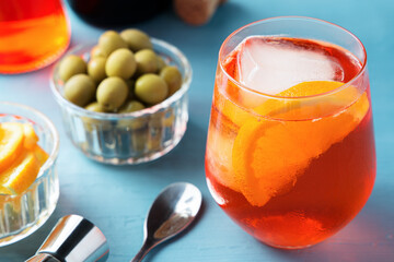 Glass of cold spritz cocktail with some olives on blue table