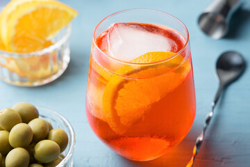Glass of cold aperol spritz cocktail with some olives on blue table