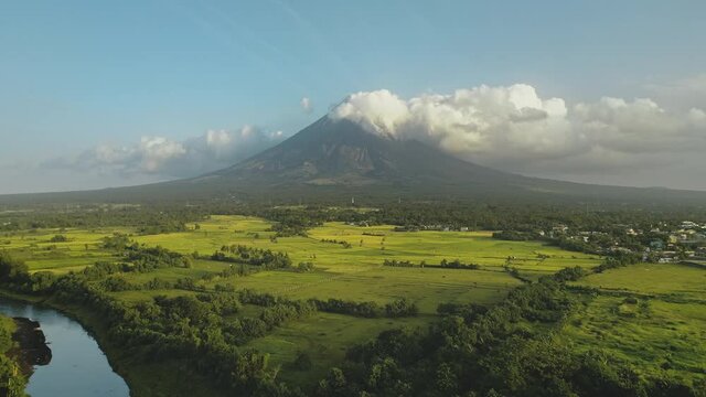 Tropic river with green banks at Mayon volcano eruption aerial. Greenery meadow at fog haze of Philippines mountain at Legazpi town. Rurar fields at stream. Filipino tourist landmark at countryside