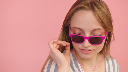 Naklejka premium Young caucasian woman with sunglasses listening to the music using headphones . Isolated on pink background, close up. High quality photo