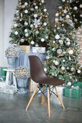 The brown chair on wooden legs costs in studio against the background of the decorated green Christmas tree and composition from cones in a vase