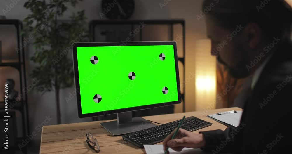 Poster view from shoulder of office worker in black suit taking notes while looking at chroma key screen of