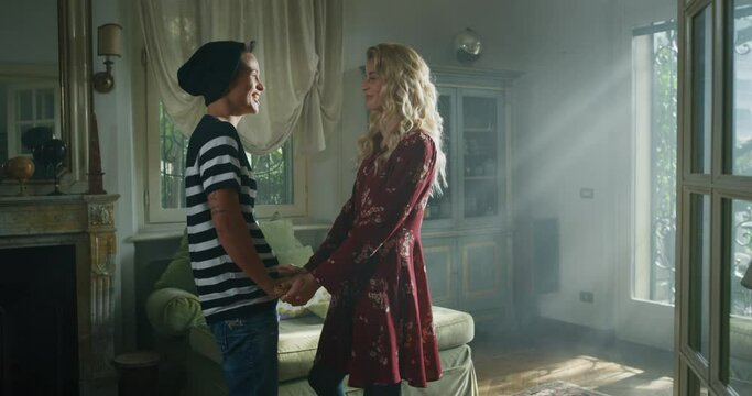 Cinematic shot of an young carefree happy smiling homosexual female gay and transgender man couple in love is enjoying to pass time together and holding hands of each other with affection at home.