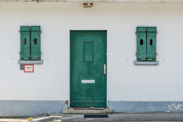 Naklejka na ściany i meble Exterior historical vintage old rough green wooden door and windows on white concrete wall.