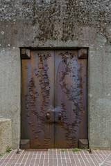 Exterior historical ornamental vintage old rough rusty iron door on raw concrete wall.