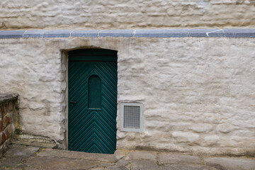 Exterior historical vintage old rough green wooden door on white stone wall.