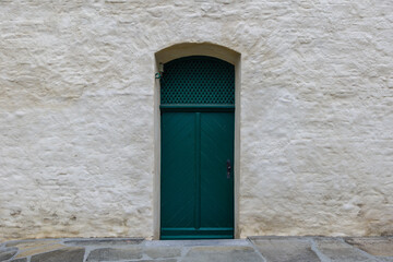 Exterior historical vintage old rough green wooden door on white stone wall.