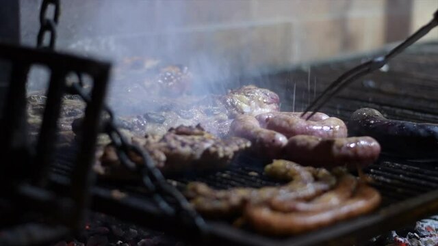 manos de mujer prepara asado argentino carne de vaca cerdo chorizo pinchado salpica morcilla chinchulines costilla mollejas  a las brasas comida tipica y tradicional cordoba argentina