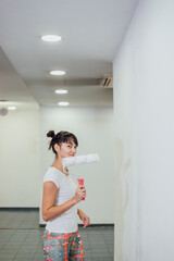 Fototapeta na wymiar Beautiful girl painting the wall with a roller. Interior renovation