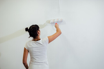 Beautiful girl painting the wall with a roller. Interior renovation