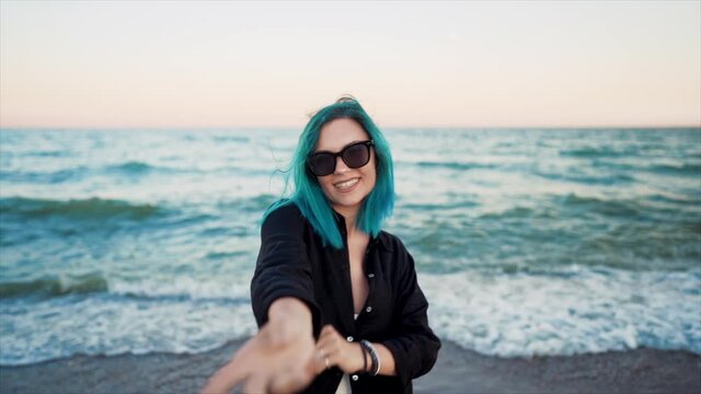 Unusual woman with blue dyed hair dancing, spinning hands around on sea background. Femininity, vacation, vitality, healthy living concept. Girl having fun, laugh.