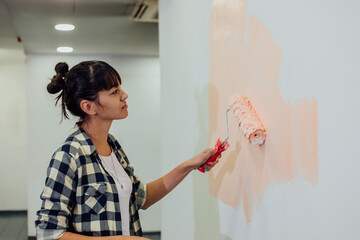 Beautiful girl painting the wall with a roller. Interior renovation