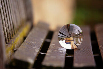 Beautiful image with lens ball on a wooden bench showing an inverted image in the sphere. Space for...