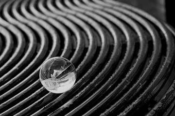 Black and white image of lens ball on a metal curved bench showing an inverted image in the sphere....