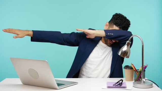 Happy positive businessman making dab gesture, moving raising hands to forehead, celebrating victory, enjoying his success. Indoor studio shot isolated on blue background