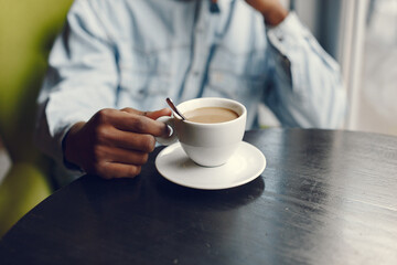 Black man in a cafe. Guy drinking a coffee. Man in a blue shirt.
