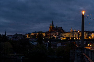 Fototapeta na wymiar railings and sidewalk for pedestrians and street lights and in the background Prague Castle and St. Vitus Cathedral at night in the center of Prague