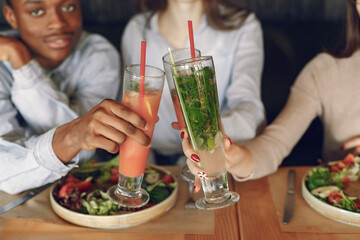 Black man in a cafe. International people. Man in a blue shirt. Women drinking a cocktails. People with a salad.