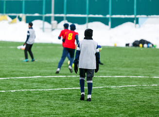 Boys in red sportswear running on soccer field with snow on background. Young footballers dribble and kick football ball in game. Training, active lifestyle, sport, children winter activity