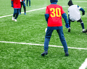 Fototapeta premium Boys in red sportswear running on soccer field with snow on background. Young footballers dribble and kick football ball in game. Training, active lifestyle, sport, children winter activity