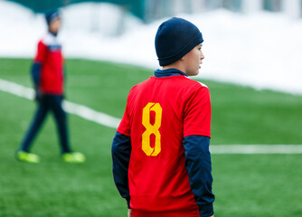 Fototapeta premium Boys in red sportswear running on soccer field with snow on background. Young footballers dribble and kick football ball in game. Training, active lifestyle, sport, children winter activity