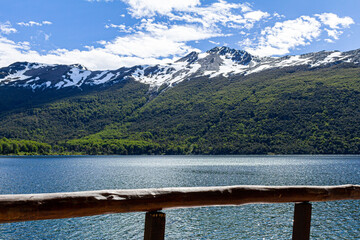 beira da varanda com uma bela vista do lago com uma grande montanha ao fundo com neve no topo e com floresta na base