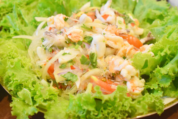 Thai called Yum Woon Sen or Spicy seafood and vermicelli salad  with shrimps, squid mixed with herbs, red chili  served with fresh vegetables side dish.