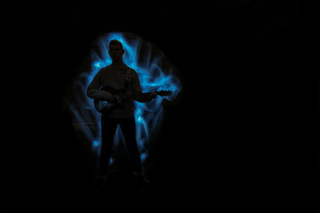 Silhouette of a man with a guitar. Lightpainting scene with a musical instrument and lighting effects in the background.